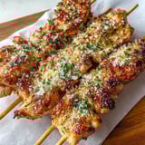 Eine Platte mit Hähnchen-Spießen, die mit Ranch-Knoblauch-Parmesan-Sauce garniert sind.