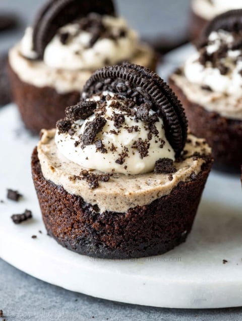A close up of a chocolate cupcake with white frosting and a chocolate cookie on top.